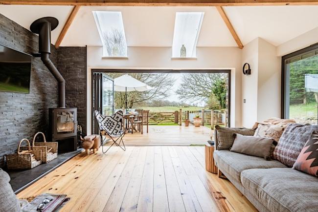 A lounge with large window at one end with views across a terrace to open fields.