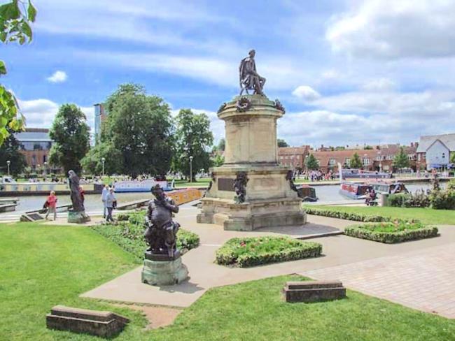 Statues in s formal garden alongside a river with narrowboats.