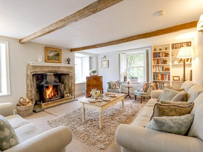 A luxurious farm cottage lounge with oak beams sofas inglenook fireplace.