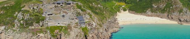 A clifftop view of sandy Porthcurno Beach surounded by rugged granite cliffs.