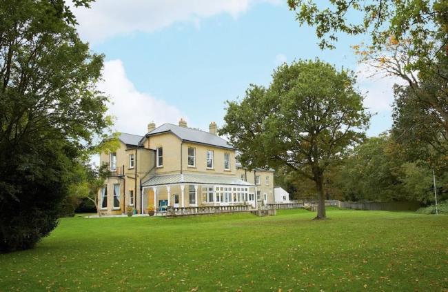 The drive and exterior of a large Isle of Wight holiday cottage surrounded by lawns.