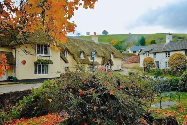 A large thatched Exmoor pub in Winsford is surrounded by trees and bushes in autumn colours.