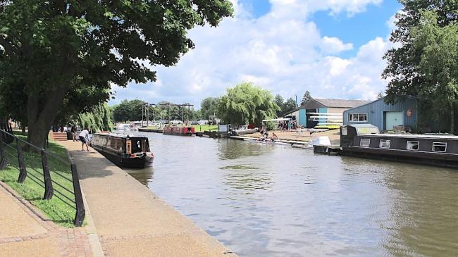 Narrowboats are moored to a towpath on a wide Fenland river.