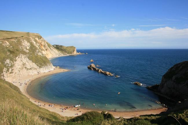 Rocky cliffs overlook a semi-circular sandy beach.