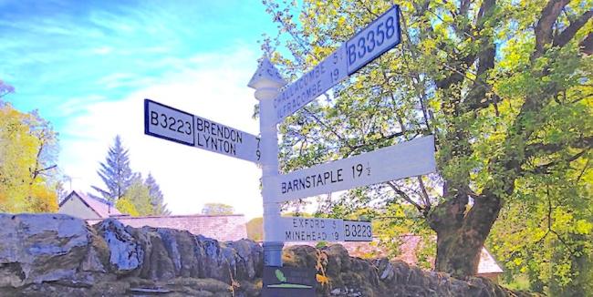 An Exmoor signpost against a backdrop of trees with several arms pointing in all directions.