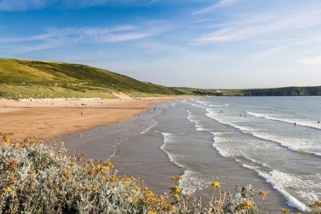 Surfing waves roll in to a long sandy beach backed by sand dunes.