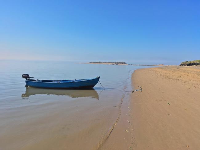 A long rowing boat anchored at the tide's edge to a sandy beach in North Devon