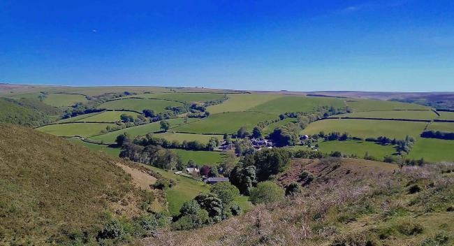 Panoramic view of a tiny village nestling in a wide Exmoor valley with fields and woods