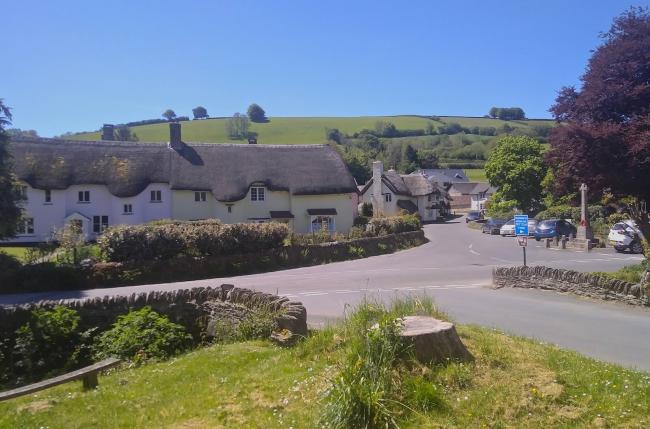 An Exmoor Village centre with thatched cottages lining a road with a war memorial.