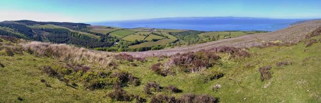 Panoramic view across moorland, fields and woods to the sea. 